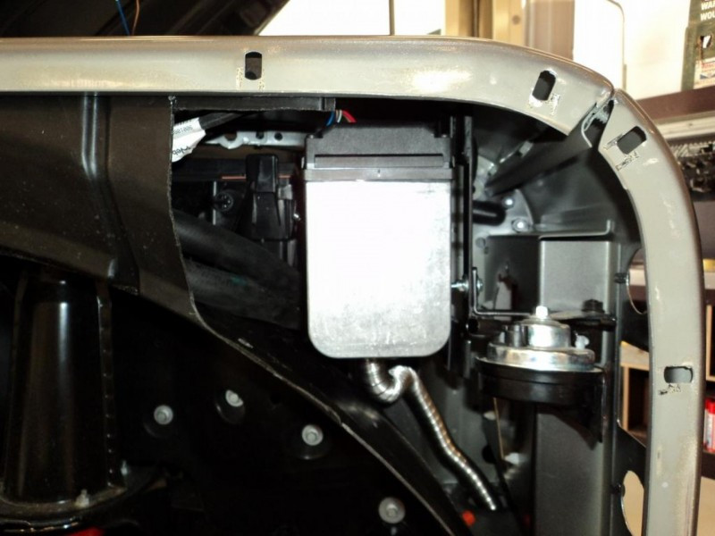 Close-up of interior machinery: a silver rectangular component with hoses and wiring inside a metal frame.