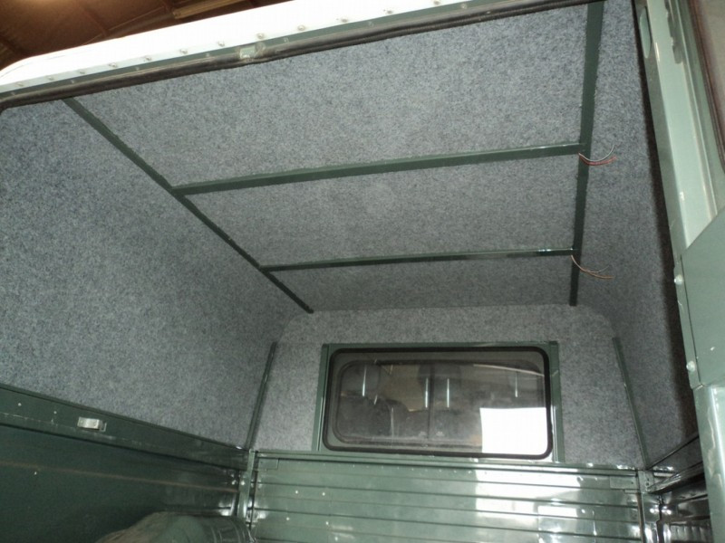 Interior of a narrow olive-green cargo space with gray carpeting on all walls and a small rear window at the far end.