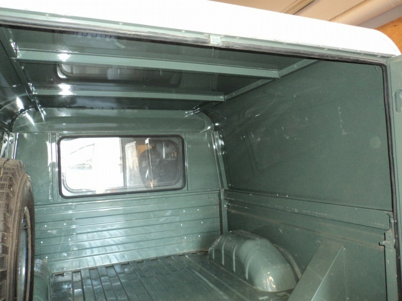 Green pickup truck bed interior with a spare tire on the left and a small side window in the cab wall.