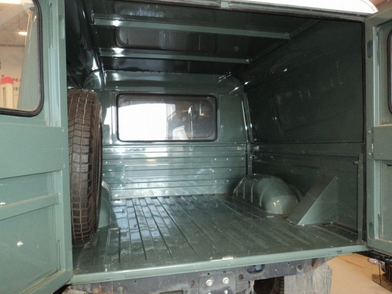 Green pickup truck with its cargo bed open, showing a spare tire mounted on the left inside the bed.