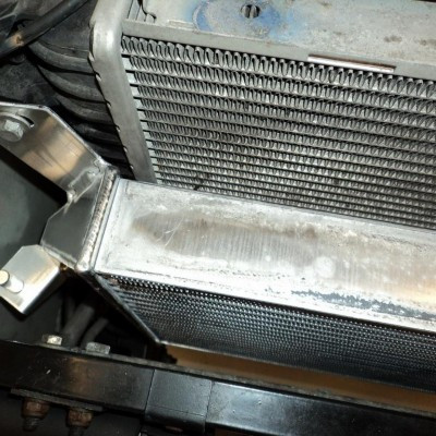 Close-up of a car radiator and metal support bar in the engine bay, with dusty fins and surrounding components.