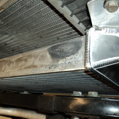 Close-up of a car radiator core with a dark stain on the metal frame near the top tank.
