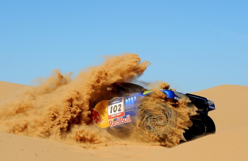 Blue rally car with Red Bull logo and the number 102 speeds through a desert, kicking up a massive dust cloud.
